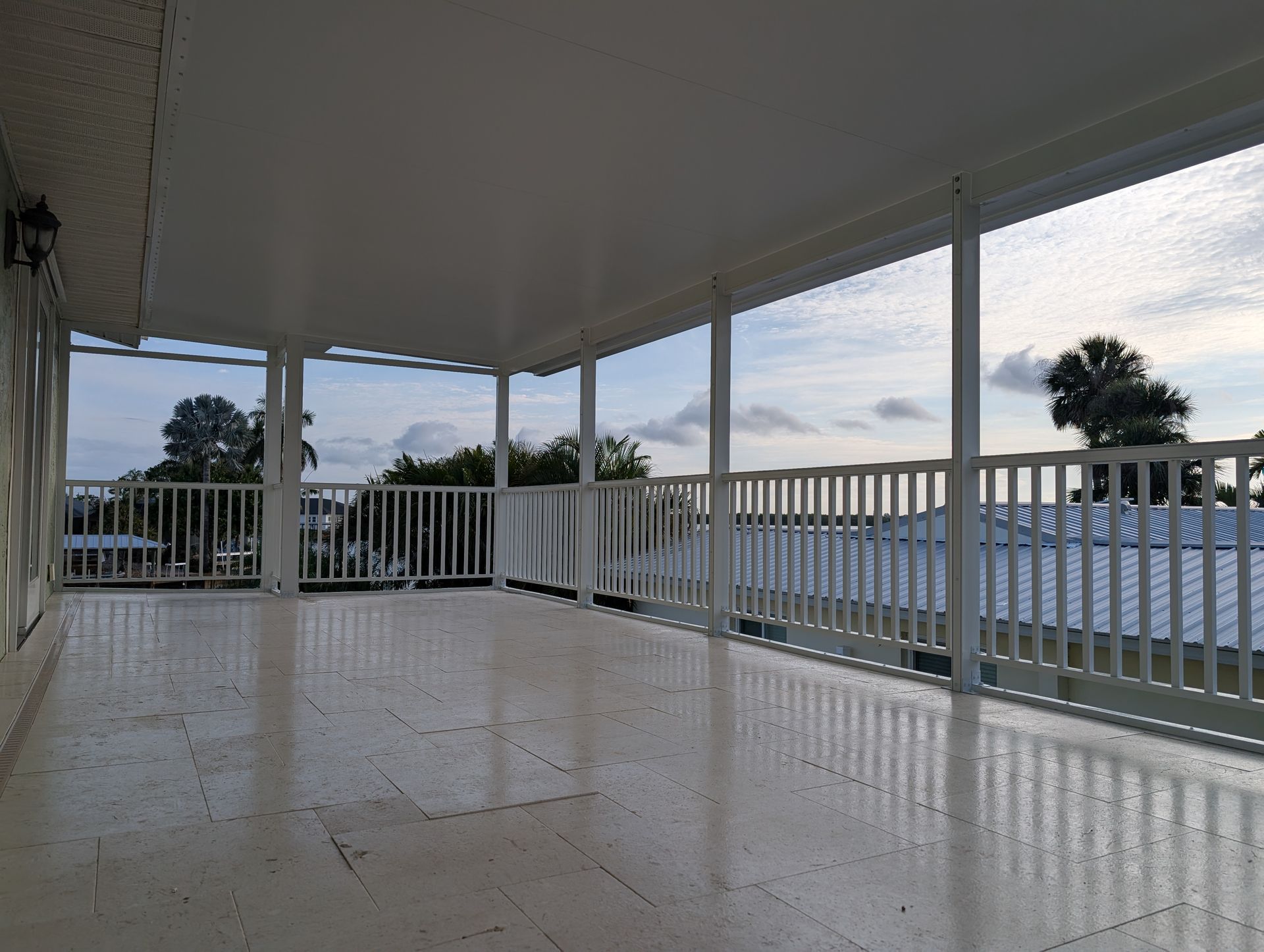 Empty screened porch with white railing and tiled floor overlooking water at sunset