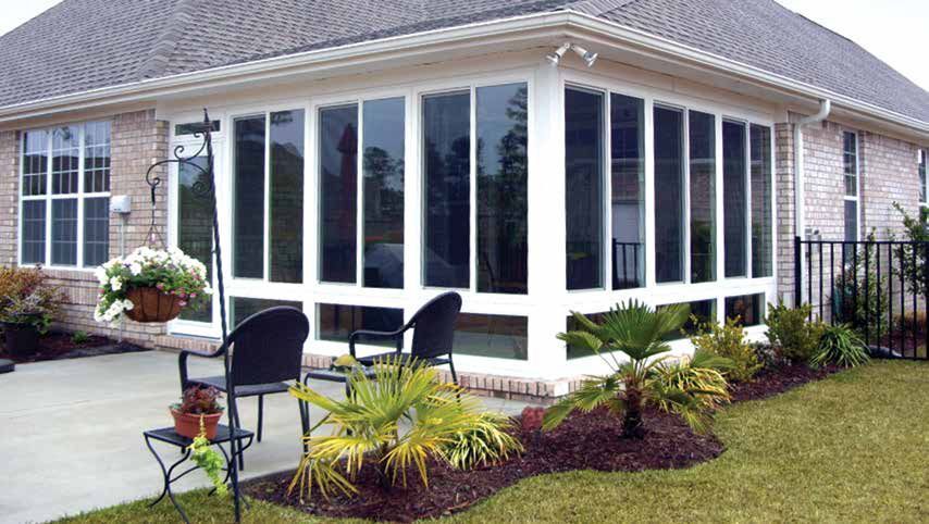 Patio with white-framed windows, black chairs, potted flowers, and a landscaped garden beside a house