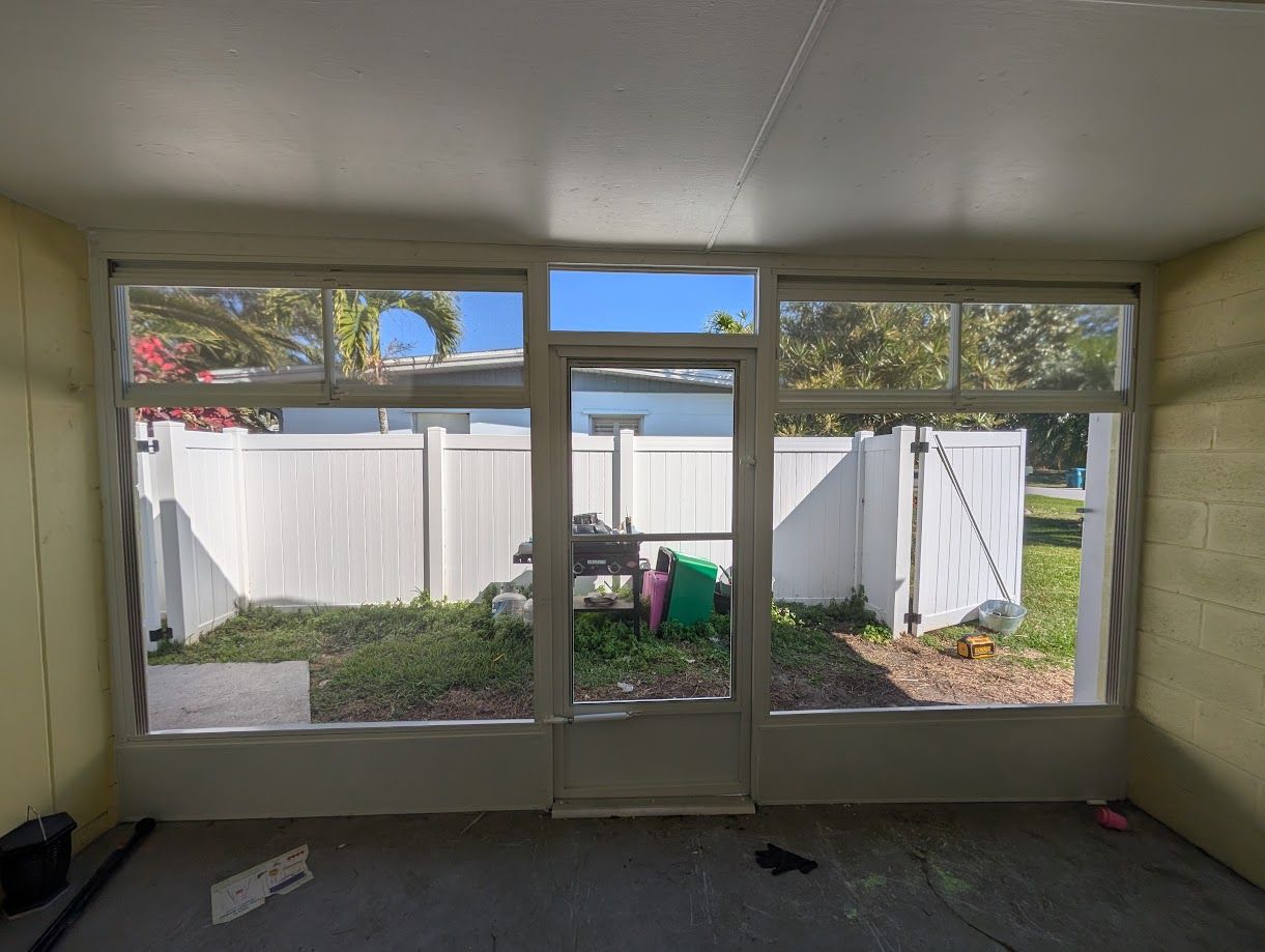 Small sunroom with large windows and a glass door overlooking a fenced backyard.
