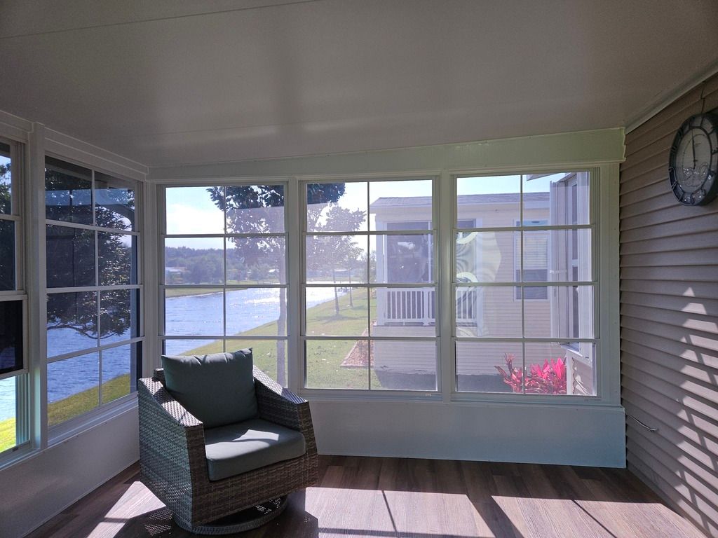 Sunroom with large windows, wicker chair, and water view beyond the lawn