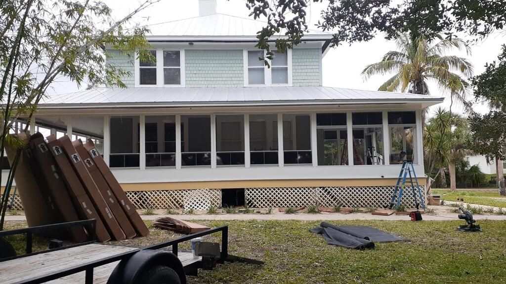 Two-story house with a screened porch and a trailer with wooden planks in the yard