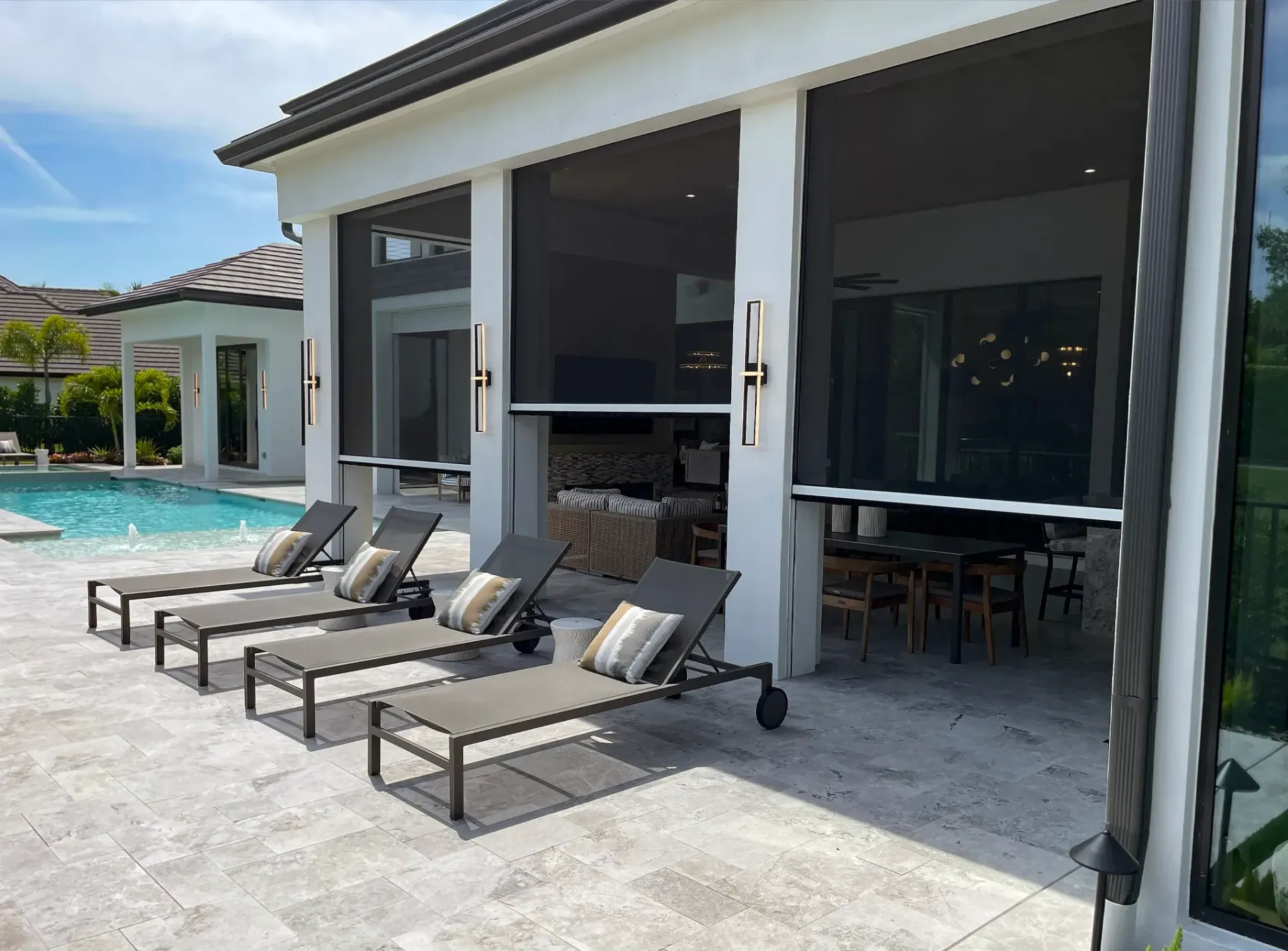 Patio with lounge chairs beside a pool, opening to a modern indoor-outdoor dining area