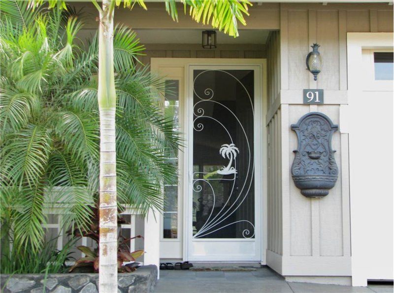 Front entrance of a house with white door, black decorative glass, palm tree, and wall-mounted mask beside number 91