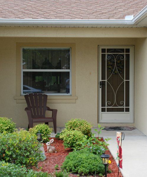 Small front porch with a chair, window, screen door, and landscaped flower bed.