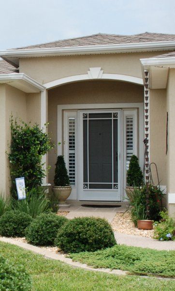Front entrance of a beige house with a white double door, arched porch, and trimmed shrubs