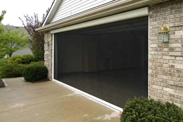 Open garage with black screen on a brick house driveway