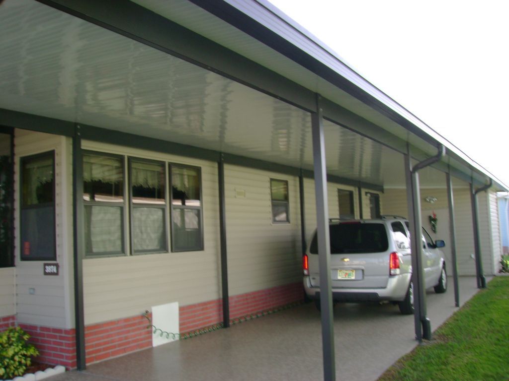 Covered driveway beside a beige house with green trim and a parked silver SUV under the carport