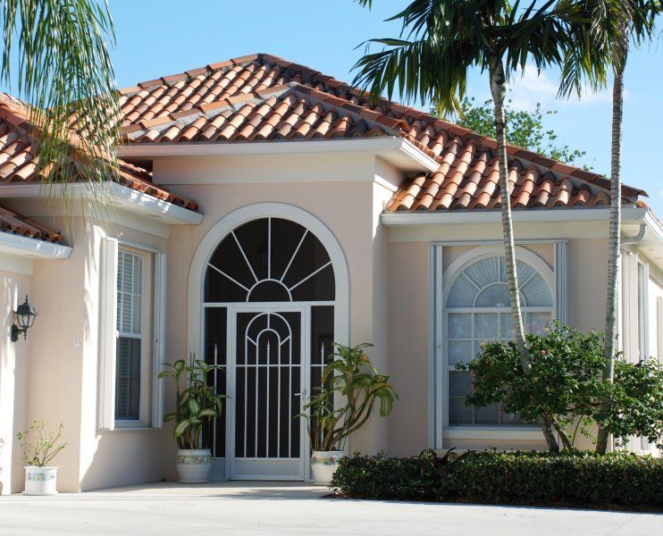 Spanish-style house entrance with arched doorway, tiled roof, and palm trees