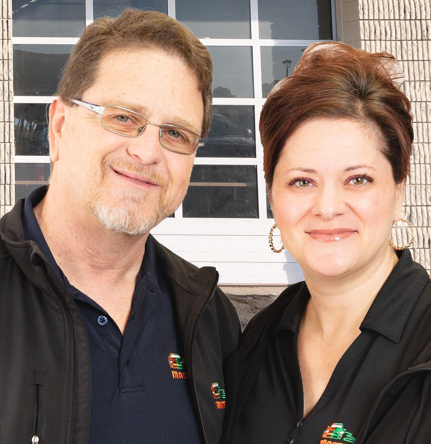 Two people in black shirts smiling in front of a white building window