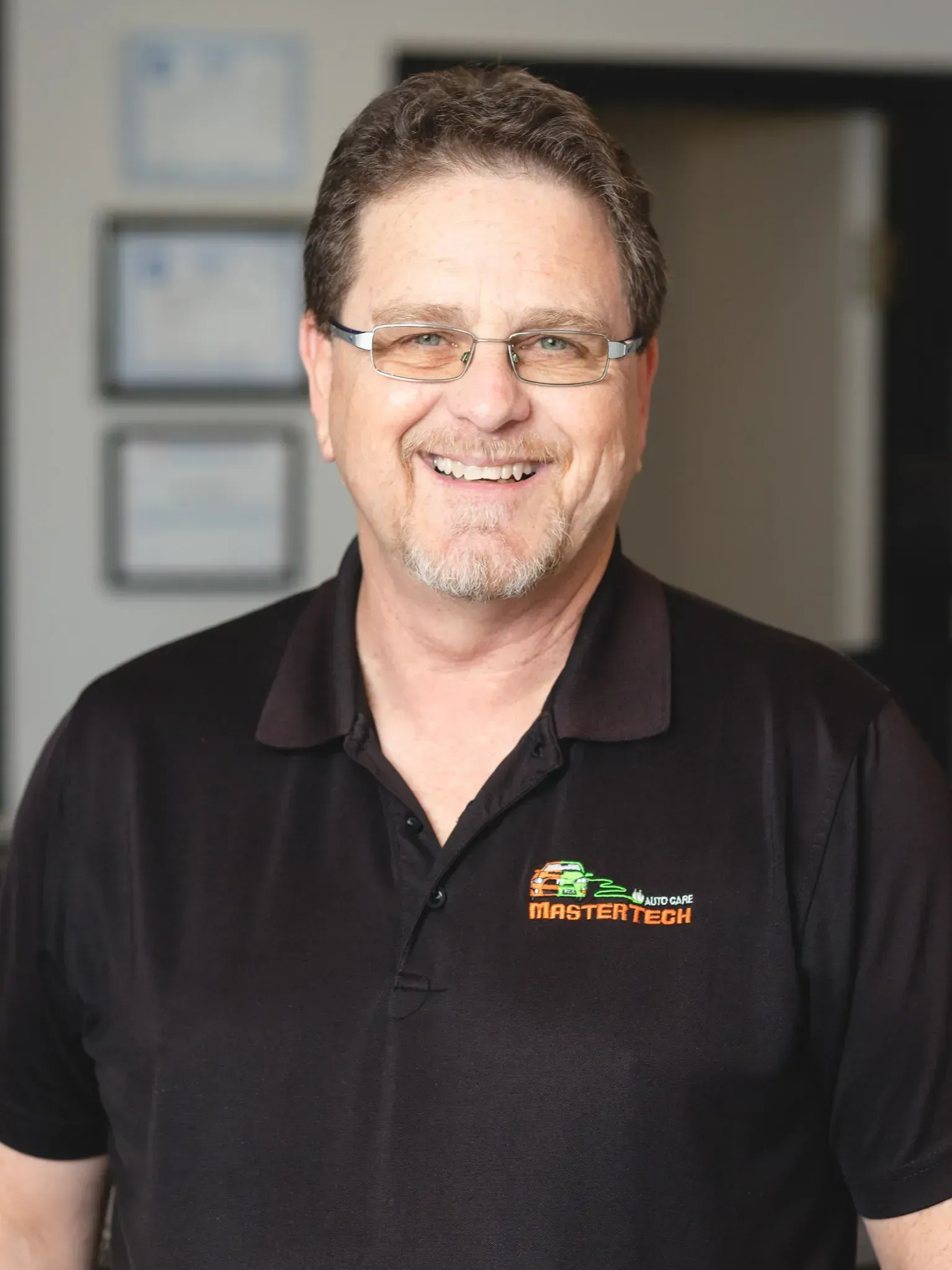 Smiling man in glasses wearing a black polo shirt in an office hallway