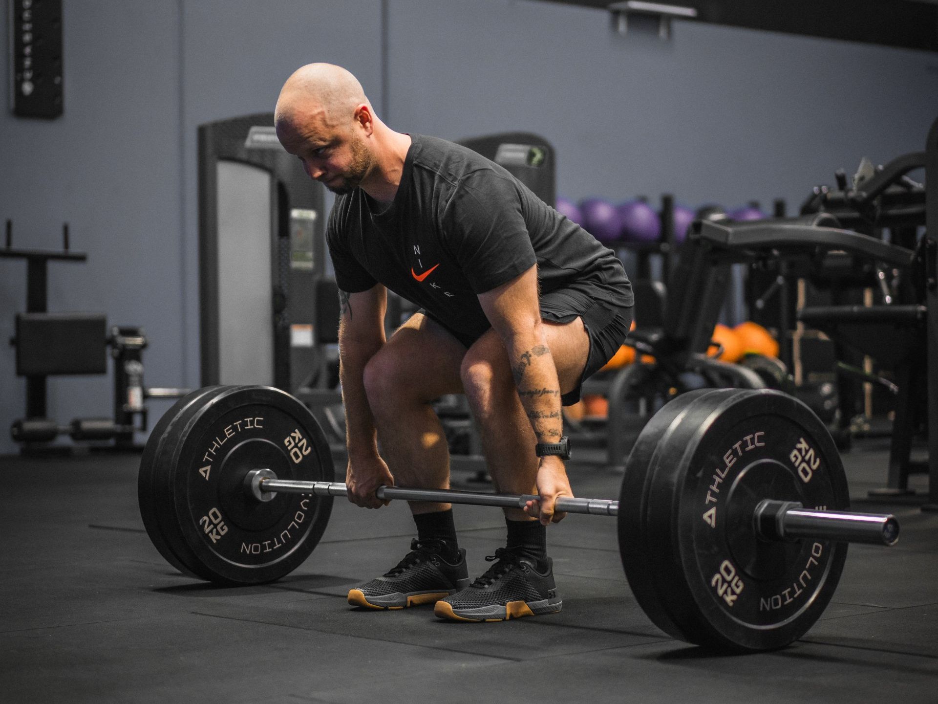 A man is squatting down to lift a barbell in a gym.