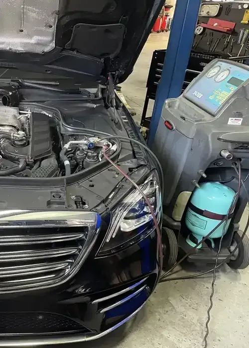 Black Mercedes in an auto shop with hood open beside a tire service machine