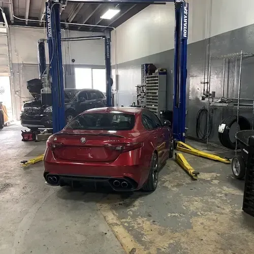 Red sports sedan on a lift in an auto repair shop, viewed from the rear.