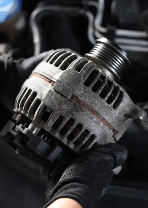 Mechanic’s gloved hands holding a used car alternator close-up