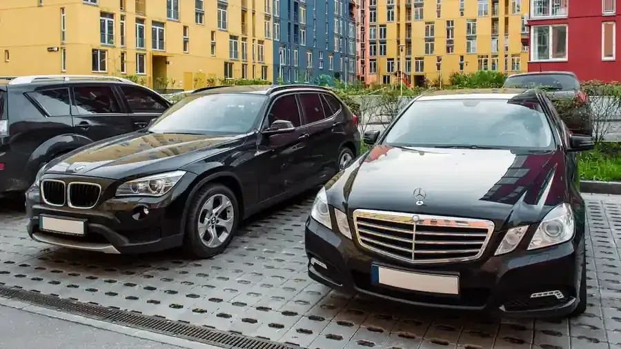 Black BMW SUV and black Mercedes sedan parked in a lot beside colorful apartment buildings