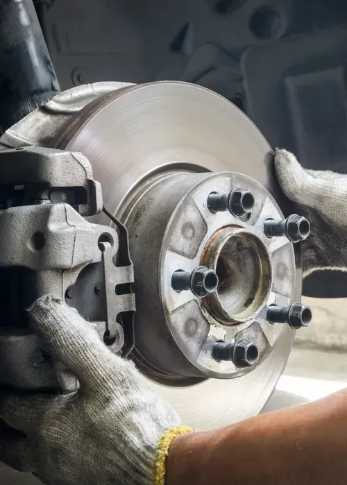 Mechanic's gloved hands inspecting a car brake rotor and wheel hub in a garage.