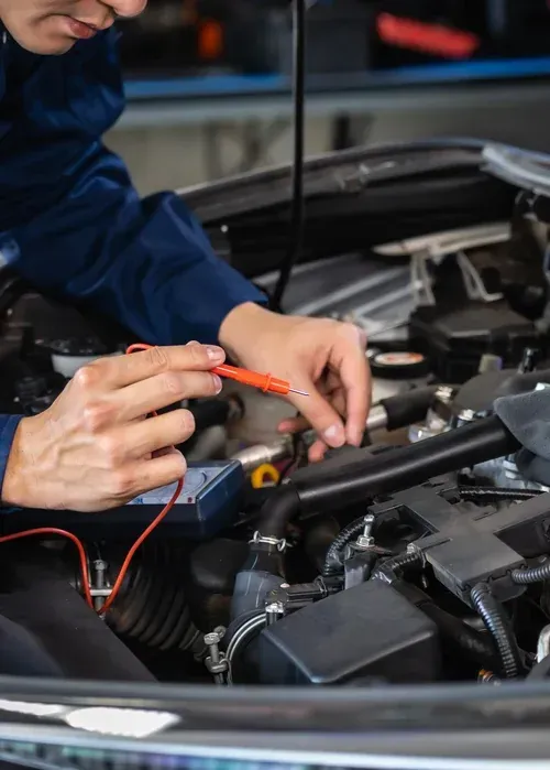 Mechanic using a multimeter to test engine components under an open car hood