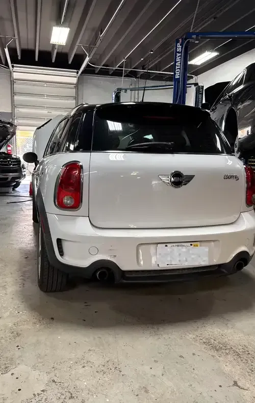White Mini Cooper parked in an indoor garage, rear view with a black roof.