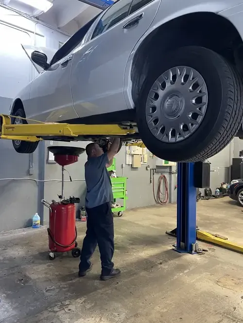 Mechanic working under a raised silver car in an auto repair shop