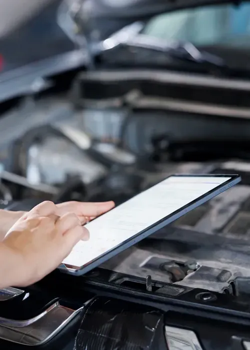 Hand holding a tablet beside an open car hood in a garage