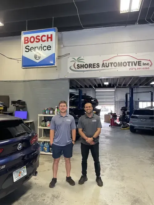 Two men standing in an auto repair shop under Bosch Service and Shores Automotive signs