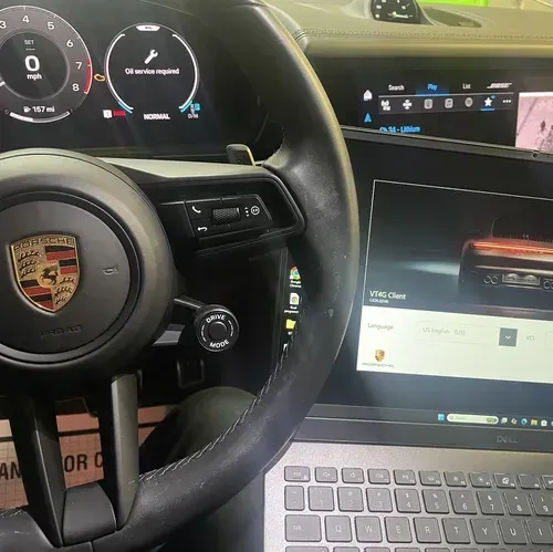 Porsche steering wheel and dashboard with a laptop open in the passenger seat.