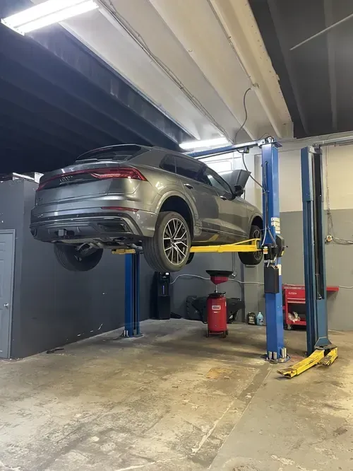 Silver SUV raised on a blue two-post lift in an auto repair shop garage