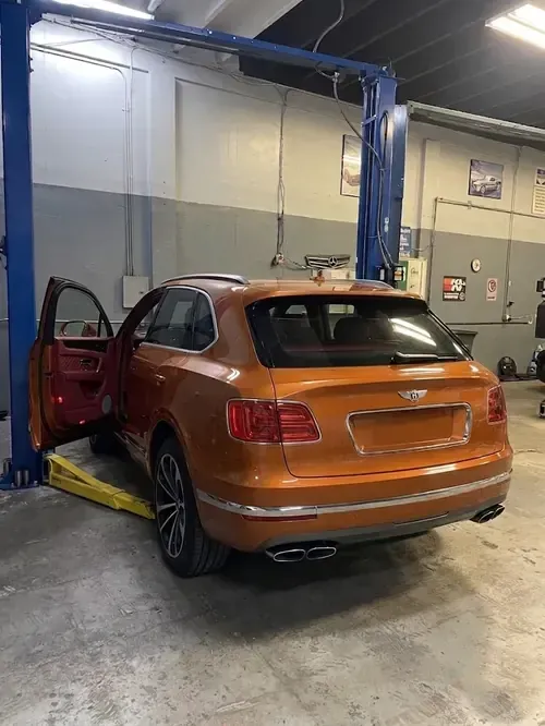 Orange hatchback on a car lift in a garage, with the driver's door open.