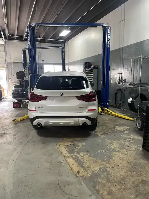 White SUV in an auto repair shop, centered under a blue vehicle lift.