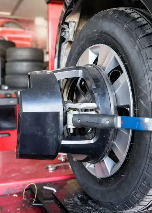 Wheel alignment machine measuring a car tire in a repair shop, with a blue clamp attached to the rim.