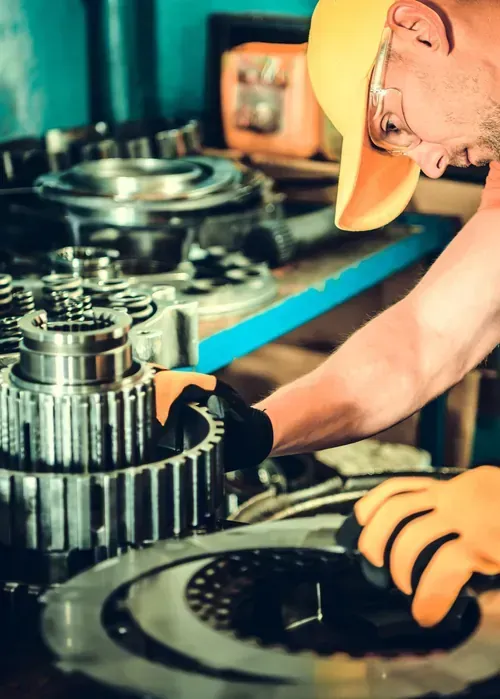 Worker in hard hat inspecting large metal gears in a workshop