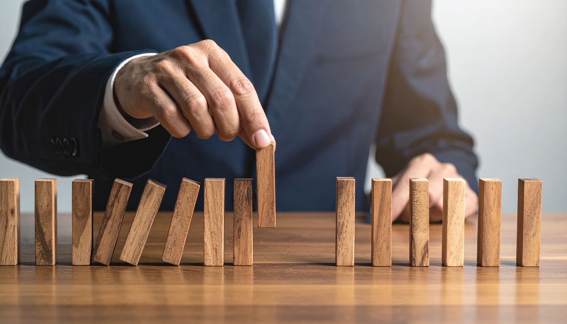 A person in a business suit prevents a domino effect by removing a wooden block from a line.