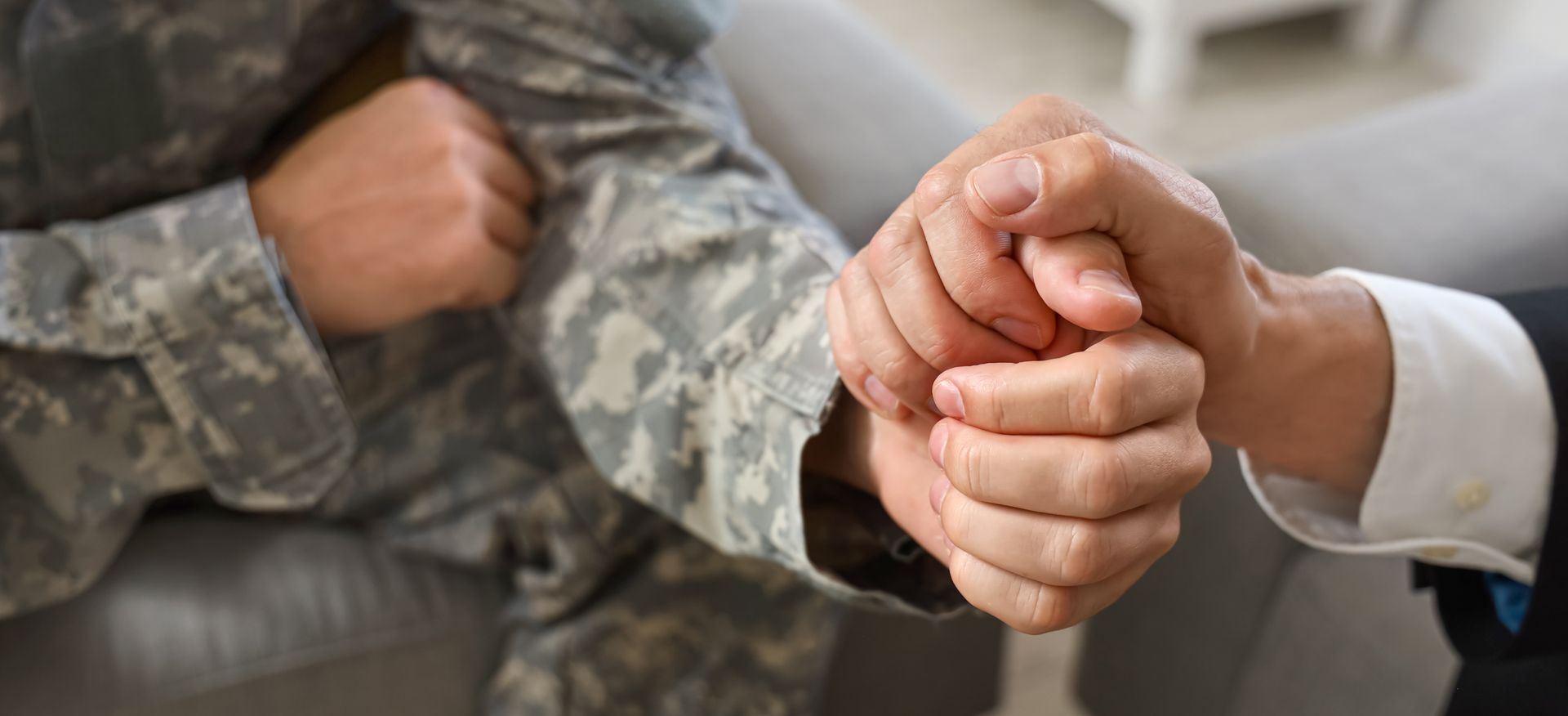A person in military uniform and a person in a formal suit hold hands in a supportive gesture.