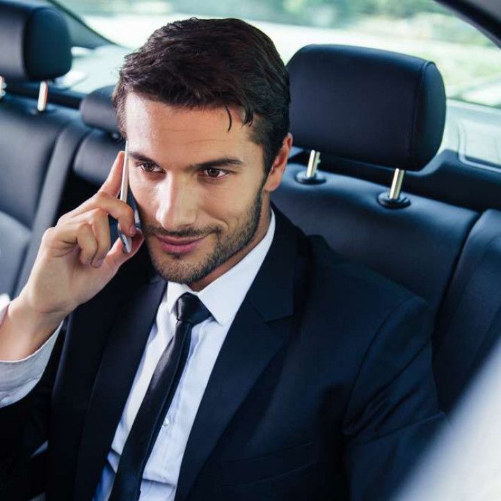 Businessman in a suit talking on a phone while sitting in the back seat of a car