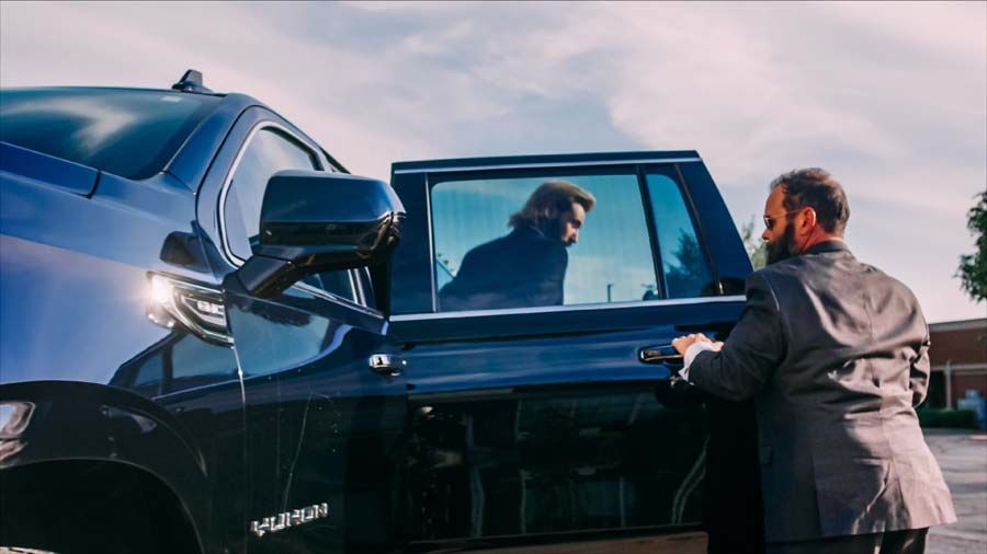 Black car with open door as a man leans in during a roadside conversation at sunset
