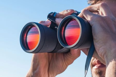 Persona che guarda attraverso un binocolo all'aperto sotto un cielo azzurro
