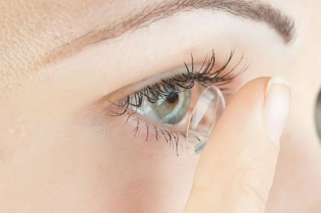 Persona che inserisce una lente a contatto trasparente in un occhio azzurro