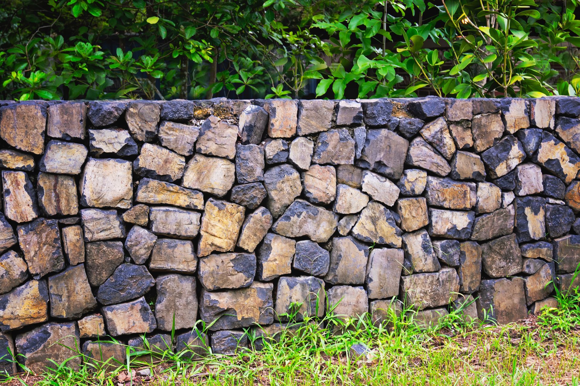 A decorative stone wall with grass and trees | Louisville, KY | S & S Concrete Inc.