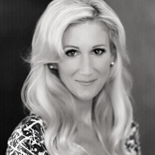 Blond woman with wavy hair, smiling, wearing a patterned top, headshot.
