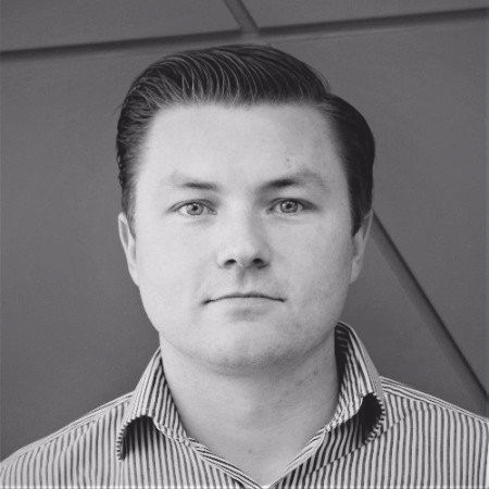 Man with slicked-back hair and striped shirt, facing forward. Gray scale photo.