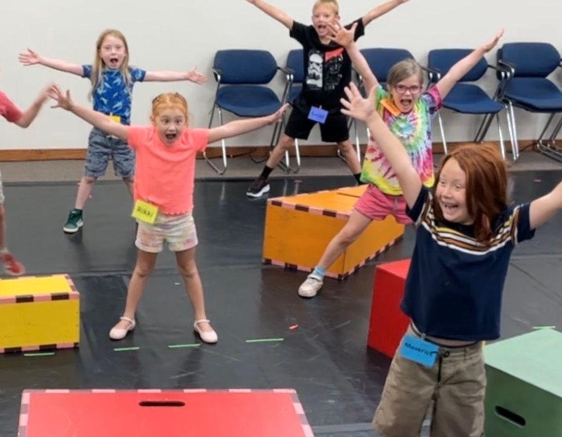 Children dancing and jumping in a classroom with colorful foam blocks and blue chairs