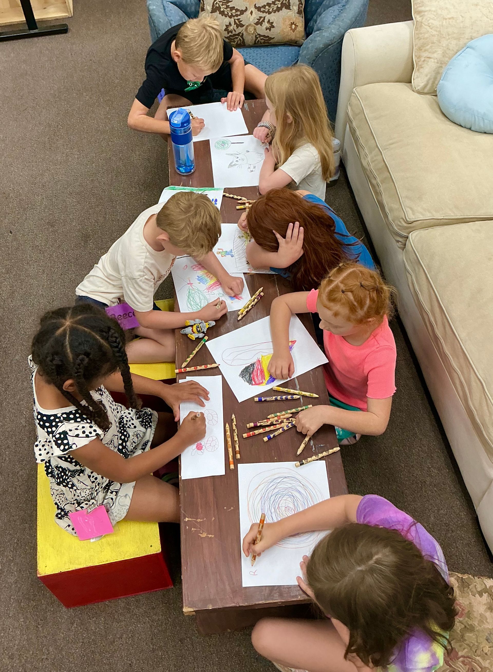 Children drawing at a low table in a living room with crayons and papers.