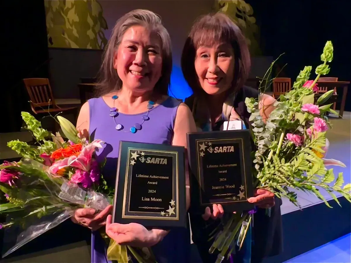 Two women are holding plaques and flowers and smiling for the camera