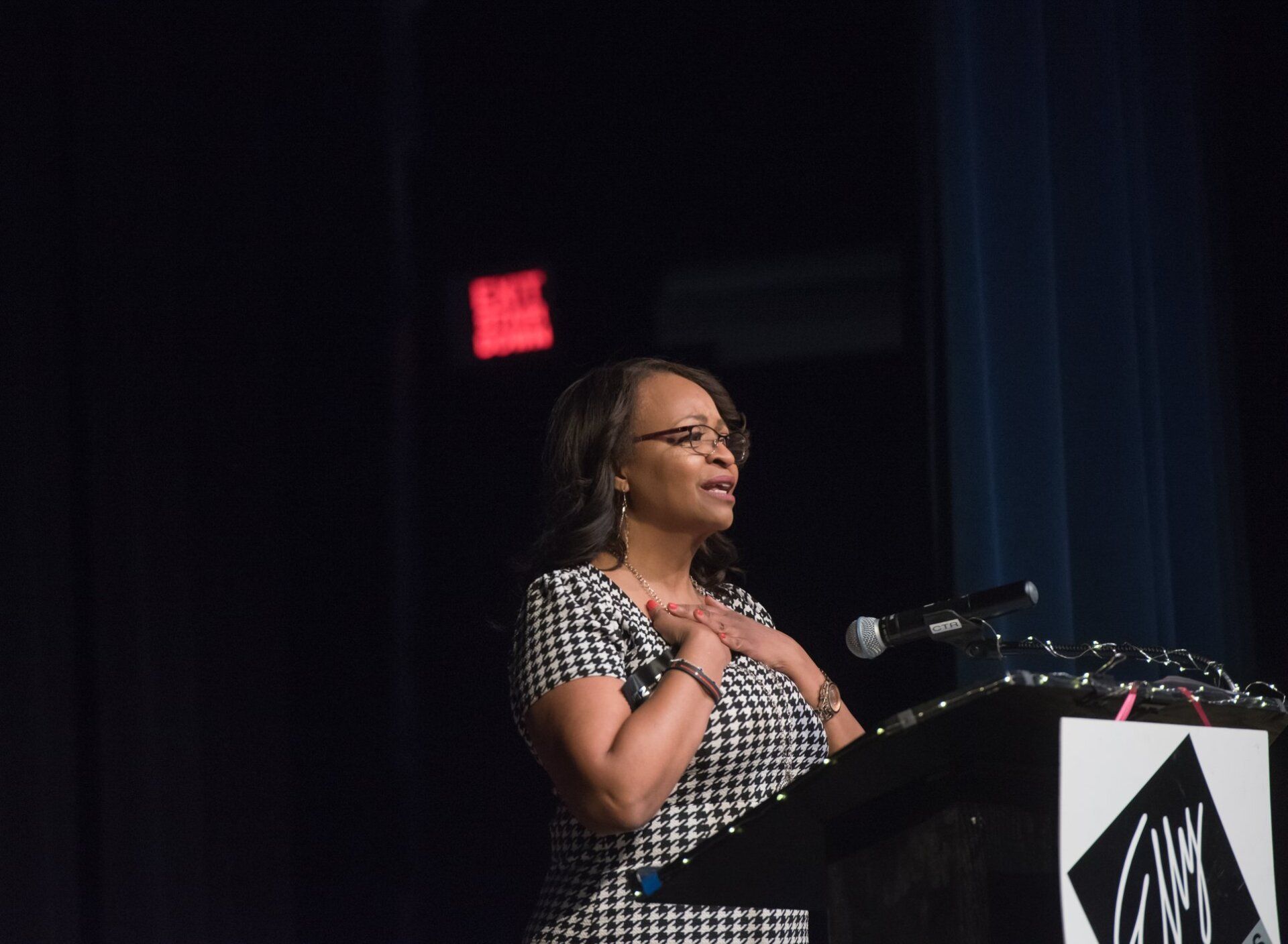 A woman is standing at a podium with an exit sign in the background