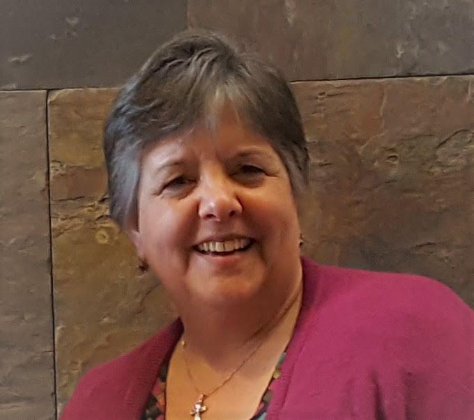 White woman with grey hair and pink shirt smiles in photo