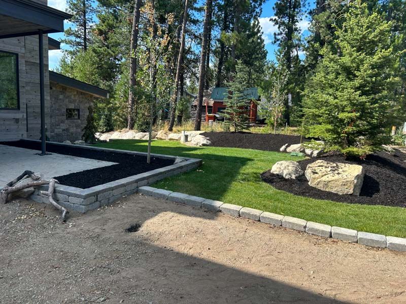 Landscaped yard with lawn, trees, and mulch beds. Stone patio and gravel path in foreground.