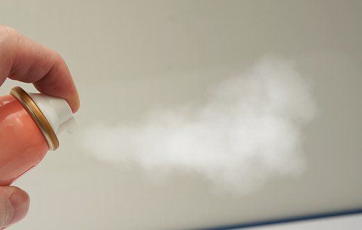 A person using a spray can to eliminate odors.