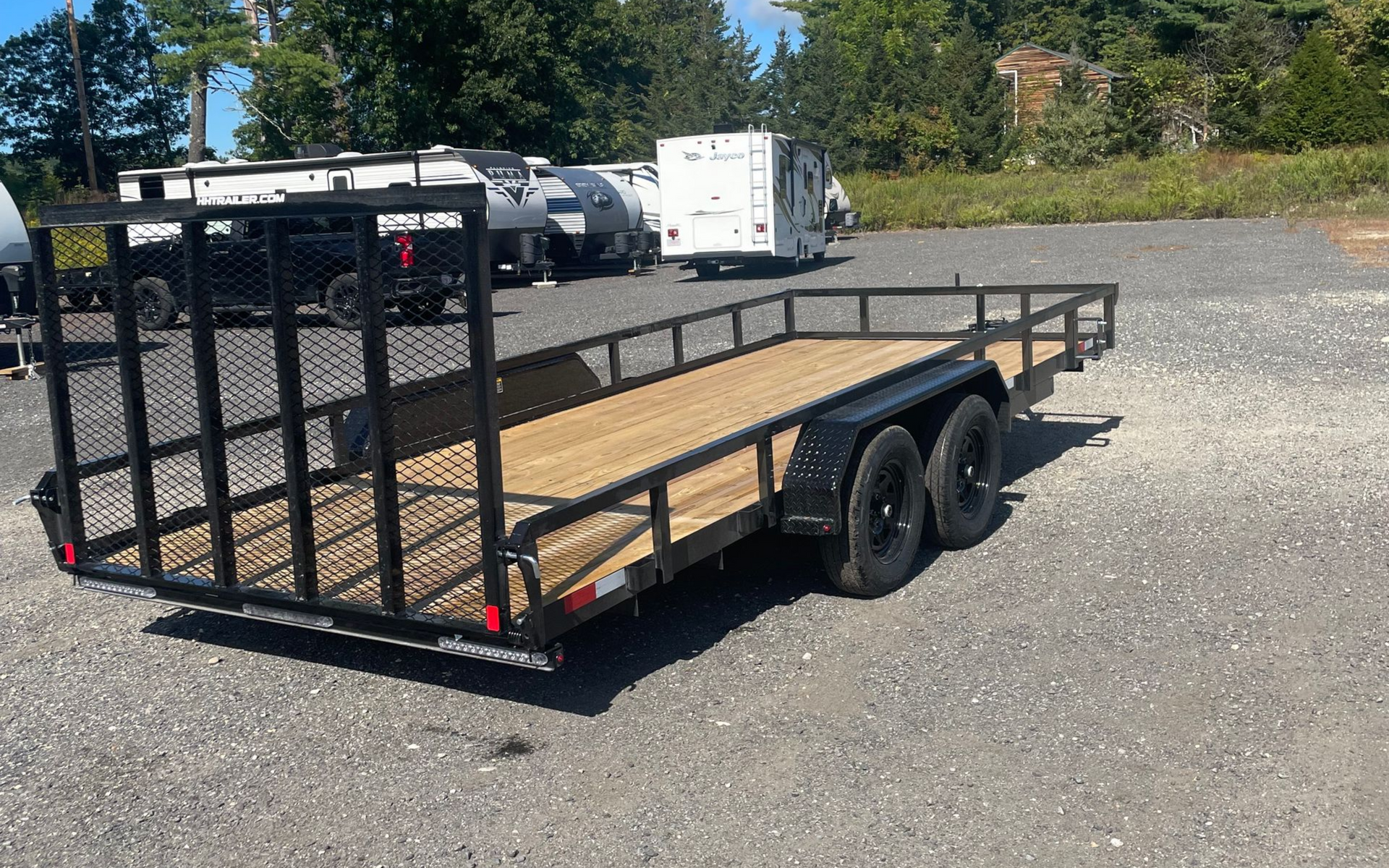Black utility trailer with mesh side railing on gravel lot.