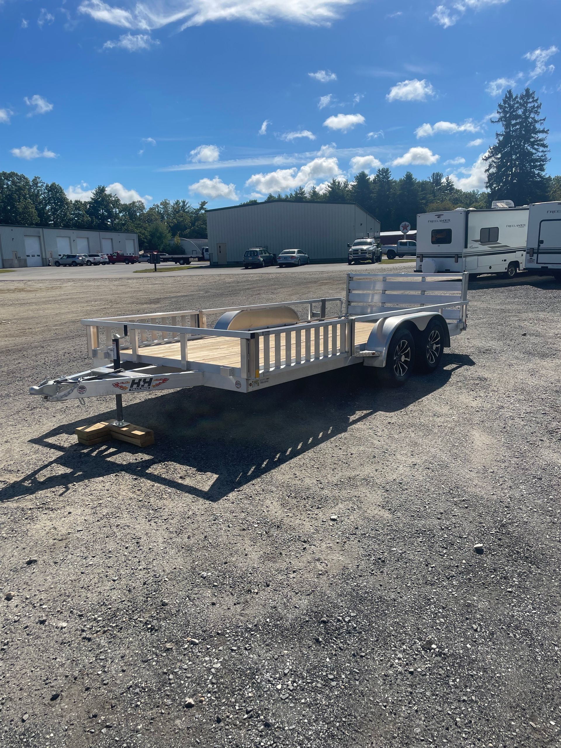 A white utility trailer parked on a gravel lot under a bright blue sky.