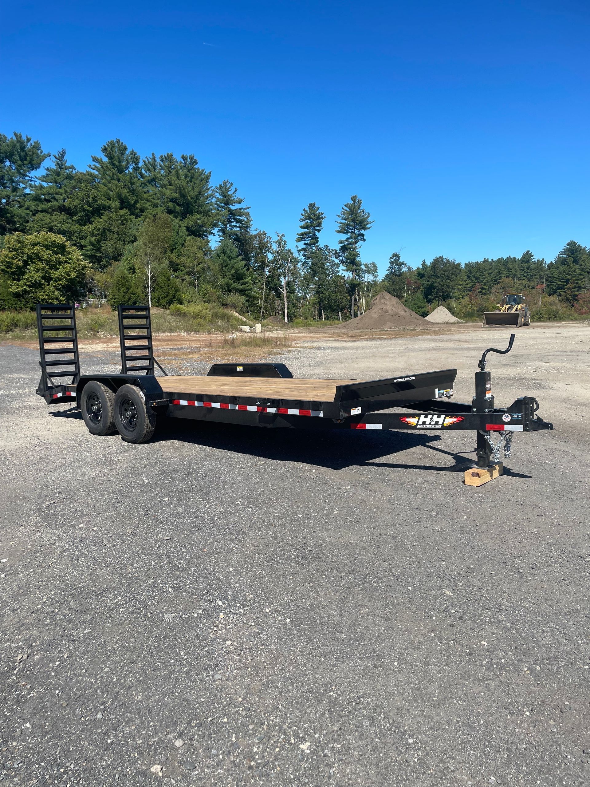 Black utility trailer on gravel with a blue sky in the background.